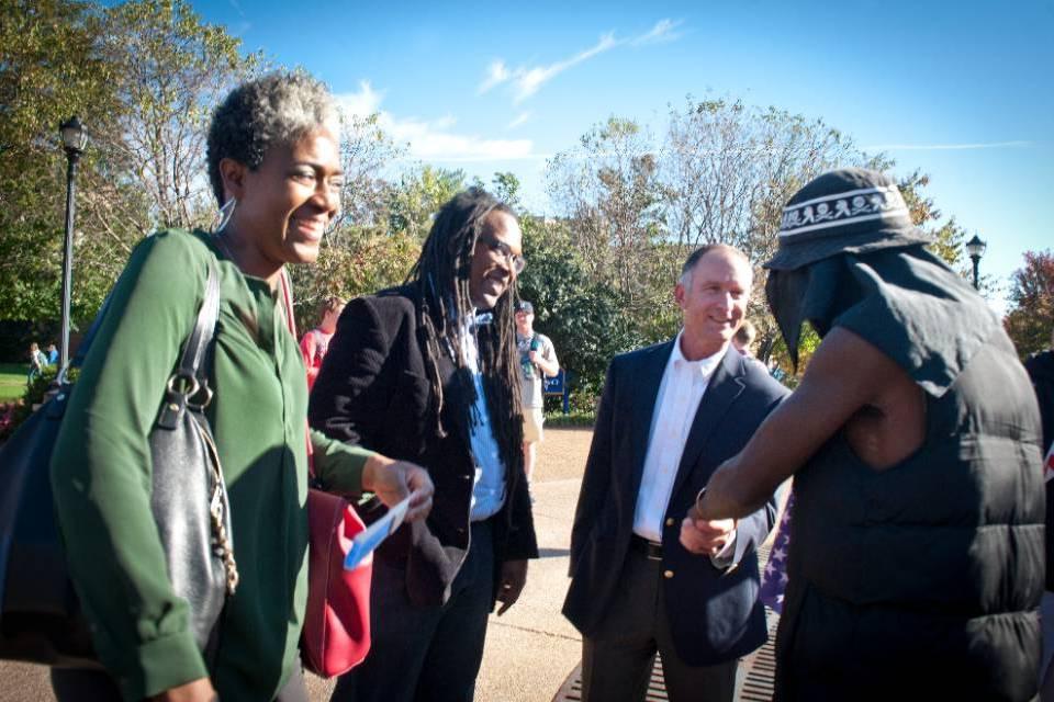 Three administrators and faculty shake hands with students.